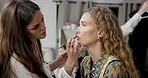 Women, makeup artist and lip gloss for model, studio and preparing for photoshoot, glow and cosmetics. Production, agency and makeover with brush for set, behind the scenes and people with equipment