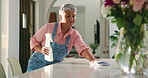 Mature woman, cleaning and cloth with spray bottle or detergent on table for housekeeping at home. Female person, maid or cleaner wiping surface with chemical for bacteria or germ removal at house