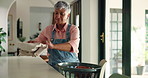 Mature woman, housekeeping and folding laundry with basket for cleaning or chores at home. Female person, maid or cleaner with smile for fabric, clothing hygiene or garment disinfection at house