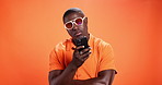 Surprise, smartphone and black man in studio, sunglasses and social media on orange background. African person, wow and model with cellphone, shades and shocked with message and notification with omg