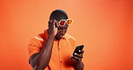 Surprise, cellphone and black man in studio, sunglasses and fraud email on orange background. African person, wow and model with smartphone, shades and shocked with message, scam and announcement