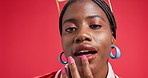 Black woman, face and lipstick with makeup in studio for cosmetics on a red background. Portrait, female person or African model with lip gloss, smile or fashion for beauty or style on mockup space