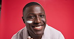 Cream, happy and face of black man for skincare, wellness and facial treatment in studio. Dermatology, spa and portrait of person with moisturizer, lotion and creme for health on red background
