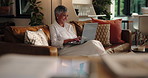 Laptop, remote work and smile with mature woman on sofa in living room of home for research at night. Computer, thinking and typing with happy freelance employee in apartment for small business