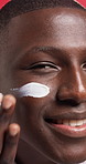 Black man, face and skincare with lotion for facial treatment on a red studio background. Male person, African model or moisturizer with smile or cream in joy for anti aging, SPF or skin protection