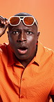 Shock, sunglasses and face of black man in studio for sale reaction, facial expression and surprise. Orange background, emoji and portrait of person for omg, fashion news and bargain announcement