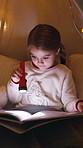 Girl, child and reading book with flashlight at night for fairy tale or bedtime story at home. Kid, relax and late evening with light or torch for novel, imagination or literature in bedroom at house