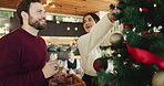 Happy couple, christmas and tree with ornament for decor or christian holiday at home. Man, woman or lovers with smile, bauble or hanging with trinkets for december celebration or festive decorations