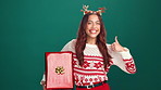 Thumbs up, christmas gift and face of woman in studio for celebration, giveaway or surprise. Happy, xmas holiday and portrait of person with present box for festive tradition by green background.