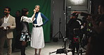 Woman, actress and makeup artist on film set with cameraman, director and staff for production. People, cosmetics and touchup with green screen, cinematography or recording equipment at movie studio