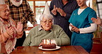 Senior woman, birthday cake and blow candles in nursing home for celebration. Party, retirement and special event with dessert, social gathering or singing with happy friends or medical team clapping