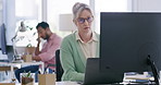 Mature blonde business woman wearing glasses while working in her office using a laptop computer at her desk. Female secretary doing admin work and looking focused while doing her job online