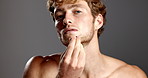 Face, beauty and man with oil for beard, shine and glow on gray studio background. Portrait, pipette and happy model apply cosmetics product for hydration, vitamin c treatment and hair growth serum