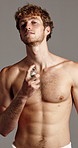 Face, cologne and man in studio, cosmetics and dermatology on gray background. Portrait, shirtless and model with perfume, person and aesthetic with beauty, aroma and fragrance bottle with grooming