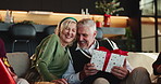 Mature, happy couple and box with christmas gift on sofa for family surprise or celebration in home. Man, woman and hug with wrapped present for december holiday, giving or christian tradition