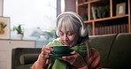 Elderly woman, coffee aroma and sofa with headphones, thinking and listen to music in lounge. Senior person, tea cup and relax on couch with drink, reflection and streaming subscription in retirement