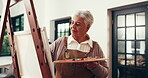 Painting, woman and smile in home, talent or artist with paintbrush for artwork, creative and craft. Happy, elderly person and inspiration for project, canvas and process with watercolor in lounge