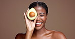 Black woman, avocado and face in studio for skincare, laugh and nutrition for beauty by background. Girl, model and happy in portrait for wellness benefits, fruit diet and mockup space in Nigeria