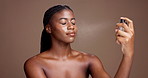 Beauty, makeup and woman spray face in studio for foundation, setting concealer and natural glow. Mockup, black person and happy with cosmetic mist application for skin hydration on brown background