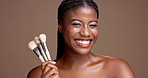 Excited, brush or face of black woman in studio for glow, makeup or skincare portrait. Happy, funny joke or African model laughing on brown background with beauty cosmetics, confidence or facial tool