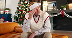 Christmas, sad and lonely senior man in home lounge for regret, memory or cancelled plans. Old person, living room and upset on festive holiday, sofa and xmas with depression or stress in house