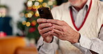 Hands, person and phone on Christmas at house for social media, browsing internet and gift search. Senior man, typing and mobile for xmas message, online shopping and reading update of festive season