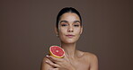 Face, woman and grapefruit for beauty in studio for vitamin c, brighten skin and natural detox. Portrait, person and fruit with organic benefits, skincare and exfoliate treatment on brown background