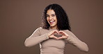 Happy woman, face or studio with heart hands for romance or love on a brown background. Portrait, female person or model with smile, like emoji or romantic gesture for valentines day or care on space