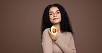 Skin care, woman and face in studio with avocado, brown background and playful attitude. Beauty, happy and female model with omega 3, collagen and natural treatment with organic facial cosmetics