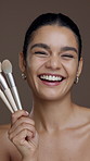 Brushes, beauty and face of woman in studio for grooming, foundation or facial glow with makeup. Happy, cosmetic tools and portrait of female person from Mexico with cosmetology by brown background.