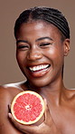 Black woman, face or skincare with grapefruit for vitamin C or health on a brown studio background. Portrait, female person or happy model with smile or natural organic fruit for antioxidant or fiber