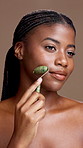 Face roller, beauty and black woman in studio for natural, health and lymphatic drainage. Portrait, skincare and African person with cosmetic tool for facial blood circulation by brown background.