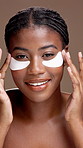 Face, skincare and black woman with eye patches for beauty, glow or health. Portrait, cosmetics and smile with collagen pads for dermatology, apply and reduce dark circles on brown studio background