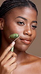 Face roller, skincare and black woman in studio for natural, health and lymphatic drainage. Portrait, beauty and African person with cosmetic tool for facial blood circulation by brown background.