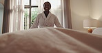 Blanket, black woman and making bed in hotel room for morning routine, maintenance and getting ready. Tourist, hospitality and cleaning in bedroom of resort for travel, vacation and holiday with robe