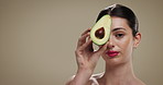 Skincare, natural and face of woman with avocado in studio for beauty, glow or moisturizing benefits. Mockup space, portrait and person with fruit for dermatology with hydration by brown background.