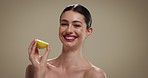 Skincare, beauty and face of woman with lemon in studio for natural, glow and facial brightening treatment. Portrait, vitamin c and person with citrus fruit for face dermatology by brown background.