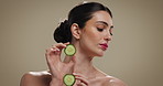 Skincare, beauty and woman with cucumber in studio for natural, glow and facial hydration treatment. Cosmetic, wellness and female person with fruit for face dermatology routine by brown background.