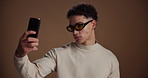 Selfie, pride and man in studio, sunglasses and confidence with fashion influencer on brown background. Space, content creation or person with stylish clothes, trendy or shades with eyewear or frames