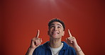 Mockup, pointing up and face of man in studio for announcement, notification and discount news. Space, happy and portrait of person with gesture for information, promotion or choice on red background