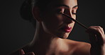 Cosmetics, brush and woman in studio with eyeshadow, beauty or facial routine with products. Makeup, self care and female person with tool for face cosmetology treatment for glow by black background.