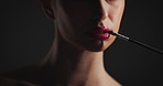 Mouth, brush and lipstick in studio for beauty, cosmetics or color application process on black background. Girl, cosmetology tools and red lips with facial makeup, self care and glow with product
