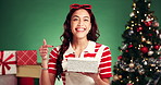 Happy woman, face and christmas with gift box in studio for festive surprise on a green background. Portrait, female person or model pointing with smile for december holiday, celebration or present