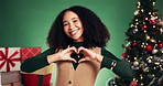 Christmas, heart and face of woman in studio for charity in festive season, holiday and tradition. Happy, xmas and portrait of person with emoji for thank you, support or donation on green background