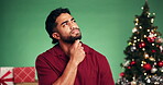 Christmas, confused and thinking with man on green background for future, planning or vision. Festive, ideas and tree with person on studio space for contemplation, problem solving or question