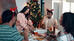 Christmas, lunch and social gathering with friends in dining room of home together for celebration. Festive, food and eating with group of happy people in apartment for bonding, holidays or tradition