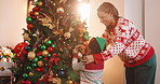 Mother, child and tree with decoration for Christmas, festive celebration or holiday tradition. Smile, woman and kid with ornaments, help and flare for family bonding and prepare xmas season in home
