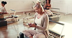 Phone, senior and woman in pilates class for fitness, reading meme or laugh on break with reformer. Mobile, exercise and person at gym club for chat, funny notification or typing text with online app