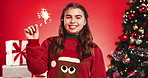Happy girl, face and christmas in studio with sparkler for festive celebration on a red background. Portrait, teenager or model with smile, joy or fireworks for december holiday or new year party