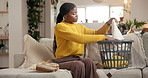 Black woman, folding clothes and basket in home, sofa and routine for chores with hygiene in living room. African person,  container and laundry with linen, fabric and cleaning on couch at apartment